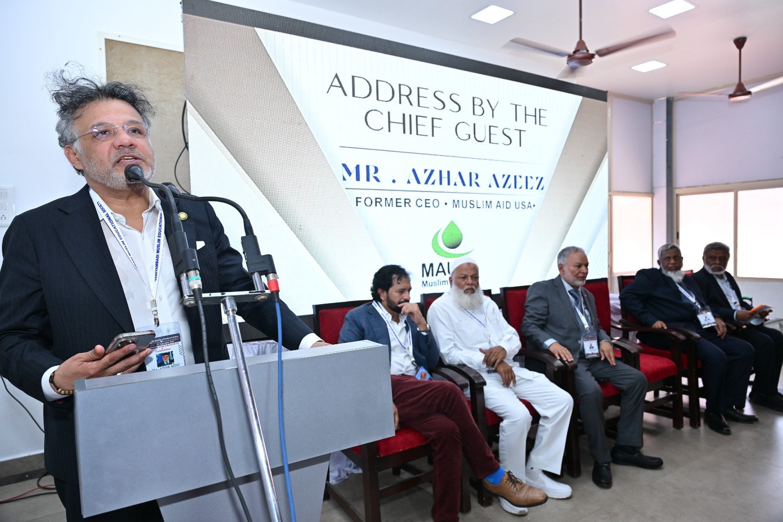 Azhar Azeez addressing an audience with educational leaders seated behind him